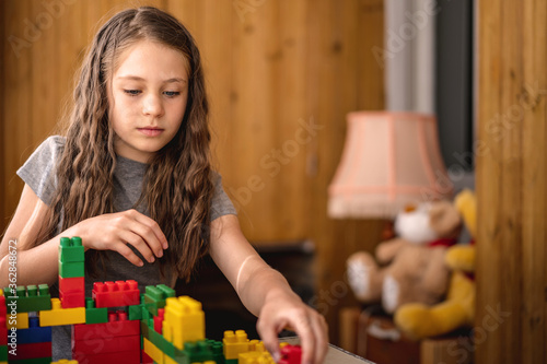 Happy little hirl child kid playing with colored plastic constructor on table in children room