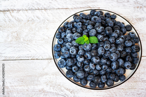 A large metallic bowl of fresh juicy blueberries with mint leaves stands on a vintage light wooden table. Summer fragrant seasonal berries. Healthy snack, proper nutrition. Top view
