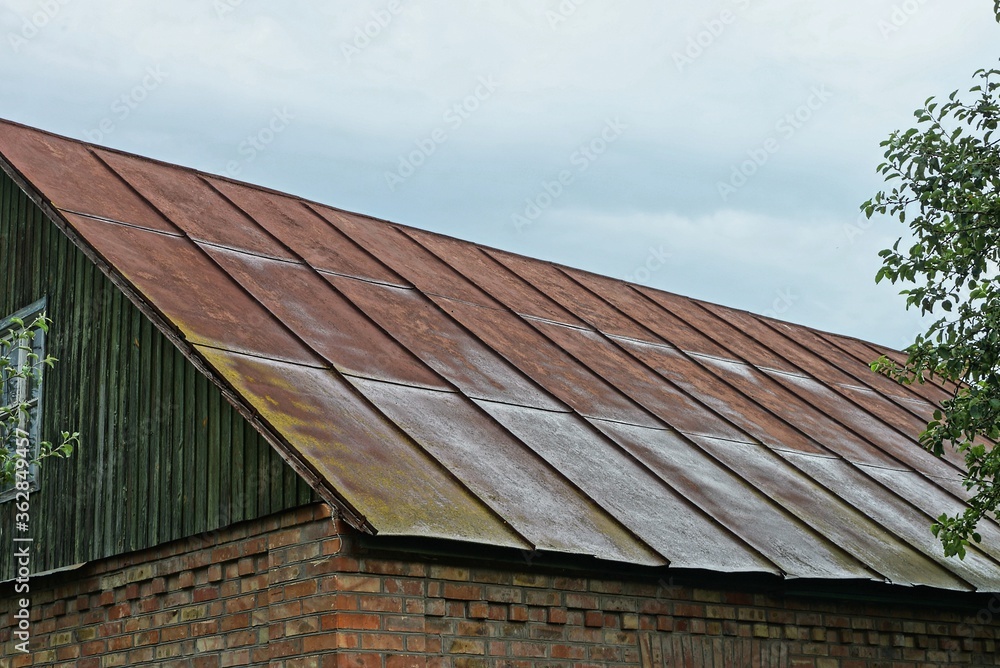 the attic of an old rural house with a rusty iron brown roof against a gray sky