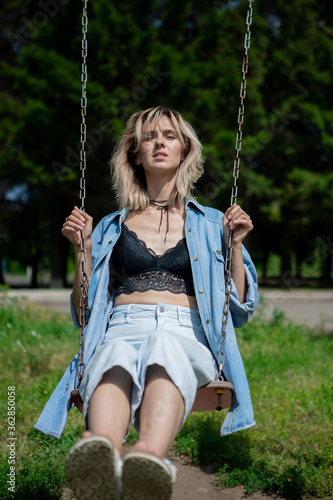 a woman swings on a swing stretching her legs. A blonde girl in a denim suit recalls her childhood