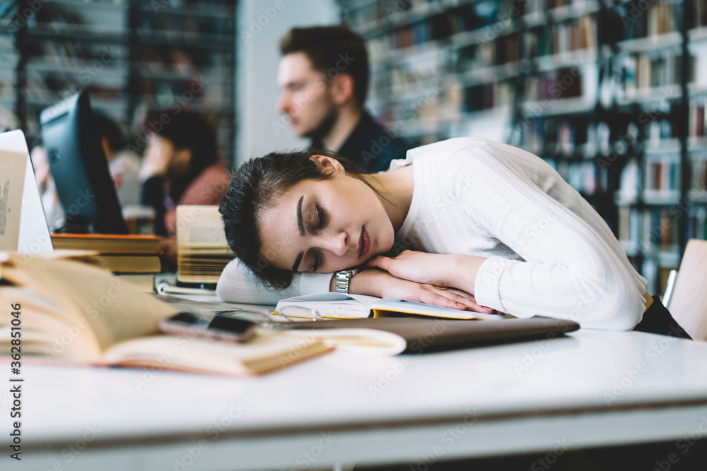 Young female woman sleeping at table with books in university library tired of learning and preparing for examinations, overworked female student need rest concept lying on desktop bored of studying. Young female woman sleeping at table with books in university library tired of learning and preparing for examinations, overworked female student need rest concept lying on desktop bored of studying.