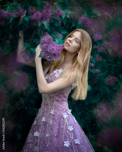 Art photo of a tender blonde girl in a lilac dress with large branches of lilac in her hands