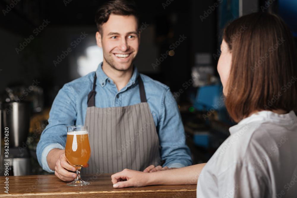 Beer for regular client. Smiling bartender gives to girl lager behind bar