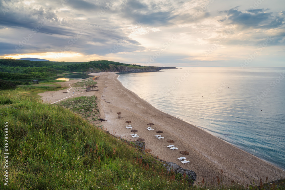 Straw sunshades and sunbeds on the empty sandy beach with sea in the background before sunset, high angle view