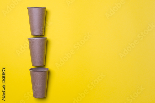 three eco-friendly cardboard cups lie on a yellow background with copy space. Mock-up. Close-up © Ganna
