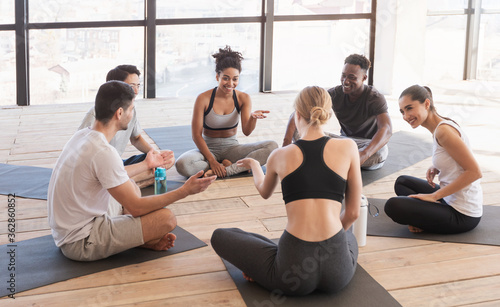 Group of young multiethnic people in sportswear having rest after yoga training