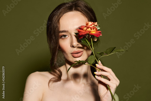 Beauty face of young woman with flower. Beauty treatment concept. Portrait of young woman with rose on green background.