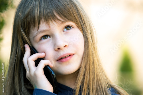 Portrait of pretty child girl with long hair talking on cell phone. Little female kid communicating using smartphone. Children communication concept.