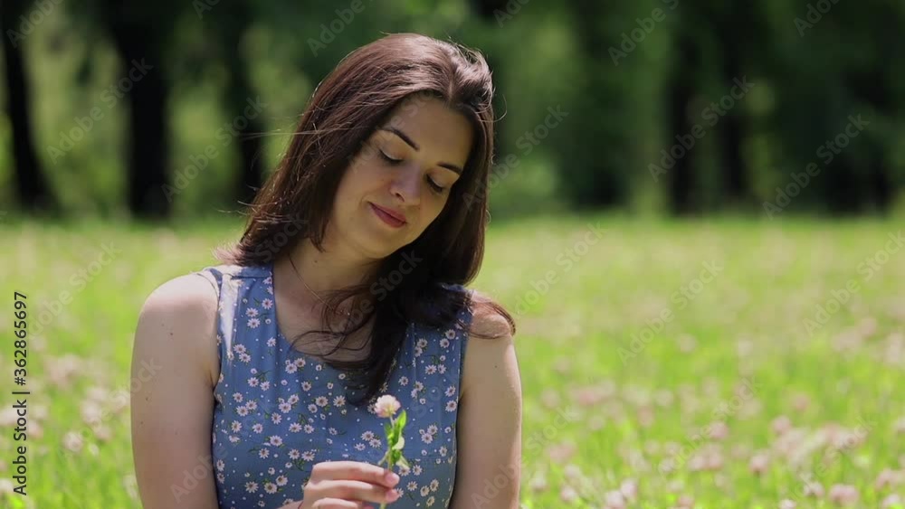 Young woman holds a plucked clover flower in her hands and smiles at her thoughts Young woman holds a plucked clover flower in her hands and smiles at her thoughts