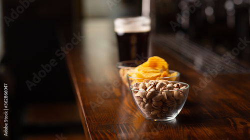 Menu for client. Pistachios, chips, nuts and glass of dark beer with foam on bar counter in interior