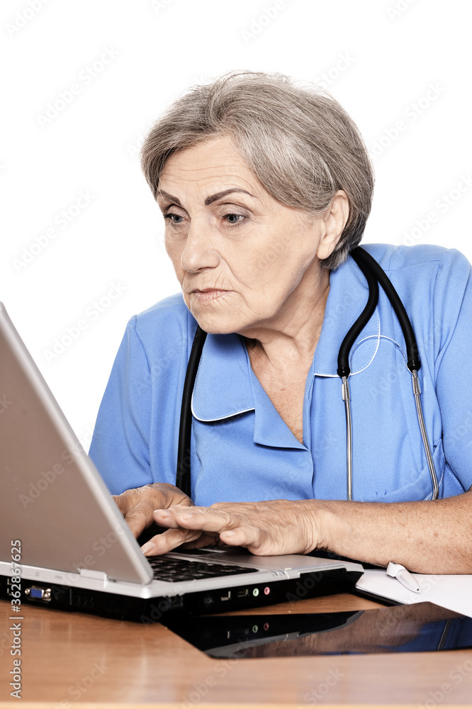 Serious elderly woman doctor sitting at table with computer Serious elderly woman doctor sitting at table with computer