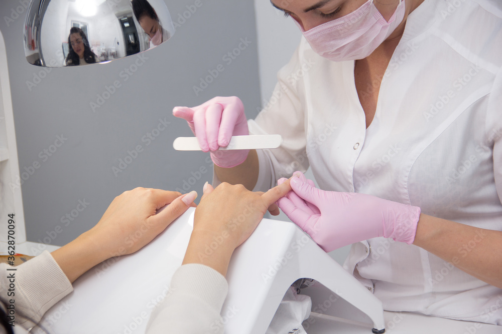 A manicurist gives a manicure to a client. Portrait of an attractive nail salon worker giving a manicure to one of her regular customers A manicurist gives a manicure to a client. Portrait of an attractive nail salon worker giving a manicure to one of her regular customers