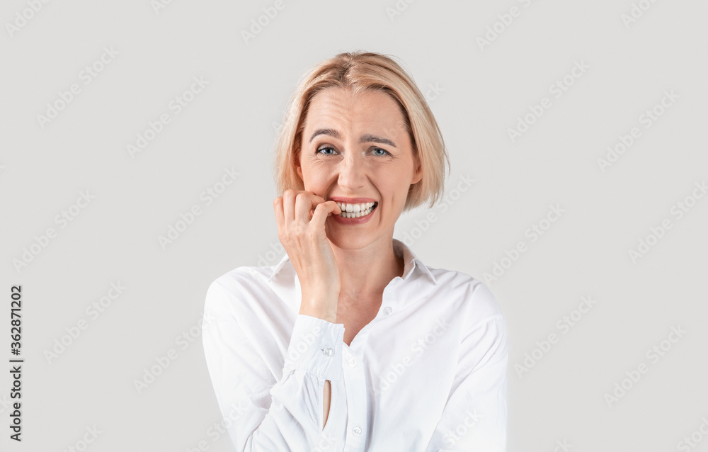 Mature secretary biting her nails in panic against light background Mature secretary biting her nails in panic against light background