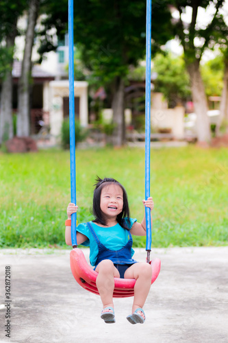 Preschoolers swing and laugh. Adorable little girl wear green and blue shirts, play on the playground. In the evening of summer or spring. A happy Asian girl is 3 years old.