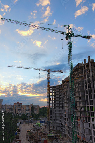 Wide-angle landscape view of construction site with two high town cranes. Construction of the new residential building. Building under construction.Beautiful sun rising sky with fantastic soft clouds