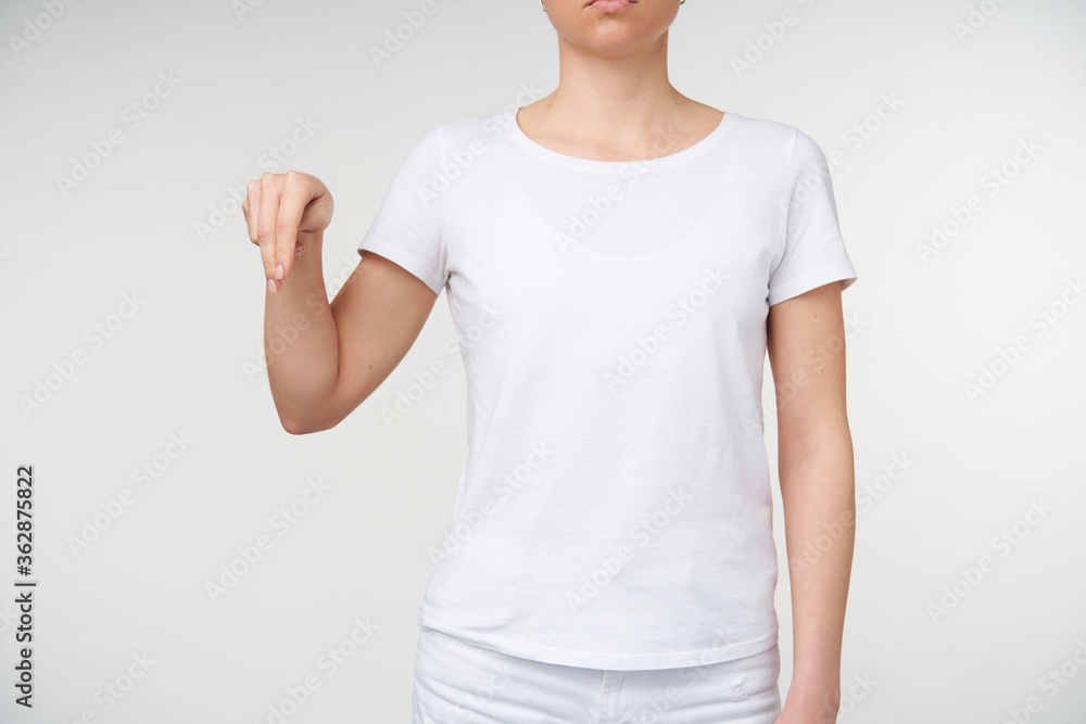 Cropped shot of young woman dressed in white t-shirt showing down with two fingers while learning deaf language, being isolated over white background Cropped shot of young woman dressed in white t-shirt showing down with two fingers while learning deaf language, being isolated over white background