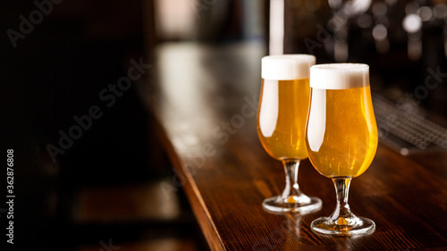 Evening at pub. Glasses with beer and foam on wooden brown bar counter in pub