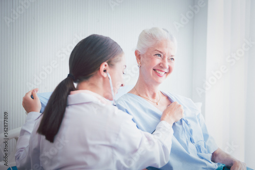 Happy Elderly patient talk with woman doctor at room in hospital. Doctor use stethoscope listening lung of elderly patient. Healthcare homecare concept