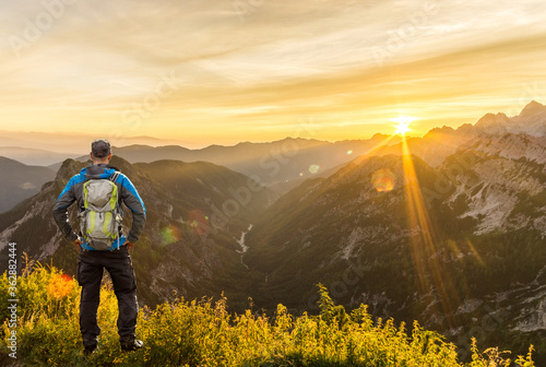 Man reaching summit enjoying amazing sunrise in the mountains. Backlight Sunlight with beautiful lens flares and sunbeams. Julian Alps, Triglav National Park, Slovenia, Mountain Slemenova, Sleme. photo