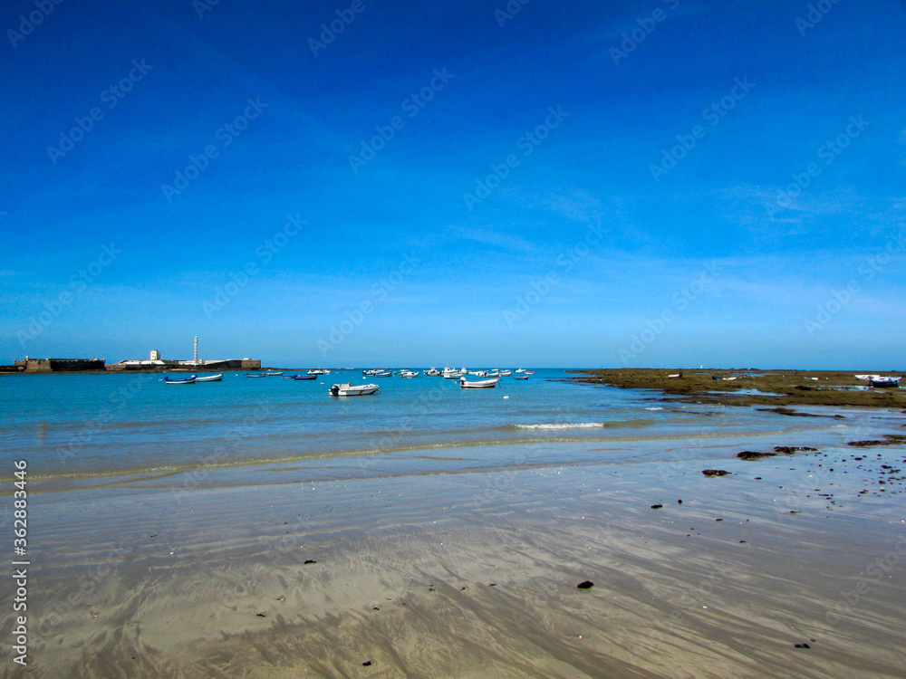 Fantastic landscape of bay on the atlantic ocean coast in Cadiz, Andalusia, Spain with fisherman boats and old castle on the background