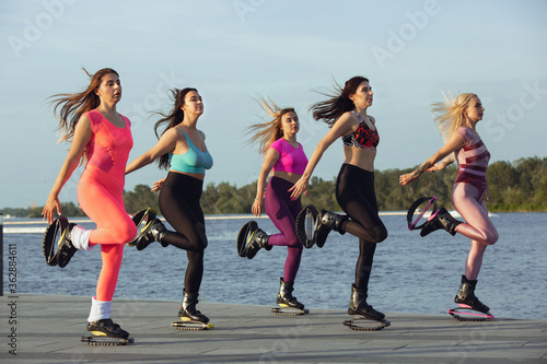 Beautiful women in sportswear jumping in a kangoo jumps shoes at the street on summer's sunny day. Jumping high, active movement, action, fitness and wellness. Fit female models during training.
