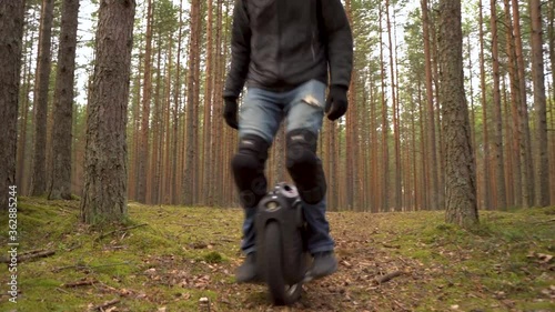 Young man riding on ecological electric transport. Adult driving unicycle scooter, balancing electric wheel through the forest. photo