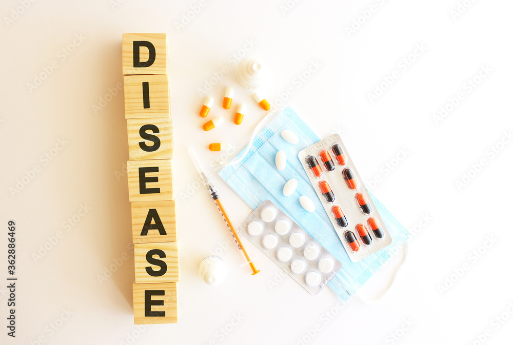 The words DISEASE is made of wooden cubes on a white background with medical drugs and medical mask. Medical concept. The words DISEASE is made of wooden cubes on a white background with medical drugs and medical mask. Medical concept.