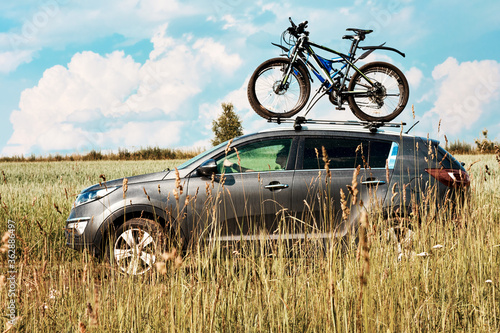 Bicycle transportation - two bikes on the roof of a car against a beautiful sky driving in the field toward adventure. A car with a mount on the roof for bicycle with two Bicycles fastened