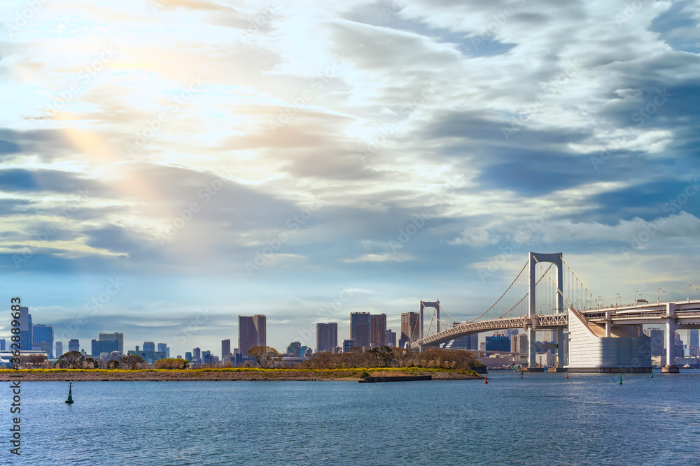 Seascape of the Bird Island of Odaiba Bay in front of the double-layered suspension Rainbow Bridge in the port of Tokyo with altostratus clouds in the sky.