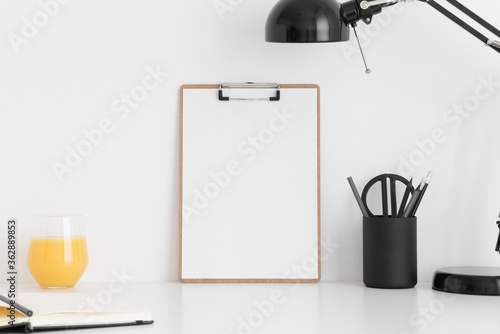 Wooden clipboard mockup wtih a notebook, lamp and workspace accessories on a white table. photo