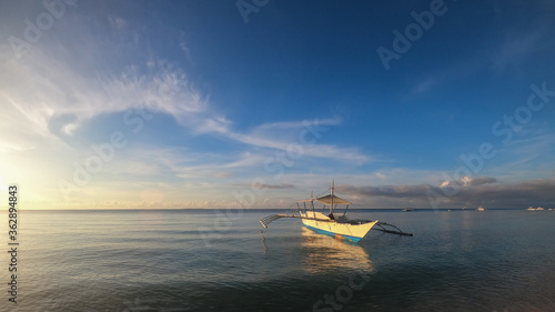 fishing boat on the surface of the sea in calm at sunset