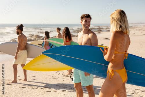 Mixed race people holding surf board on beach