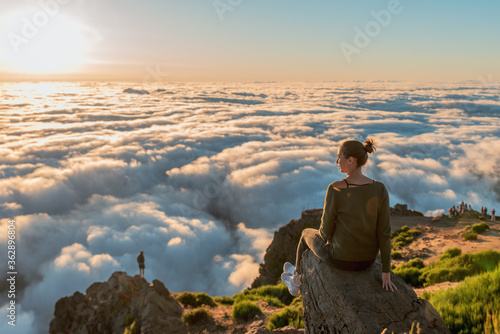 Woman on top of a summit watching the sunrise over the fluffy clouds  