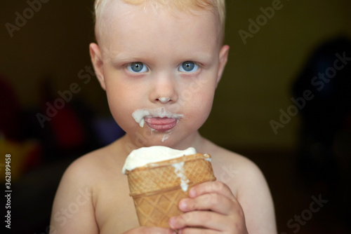 Little blue-eyed fair-haired boy eats ice cream.