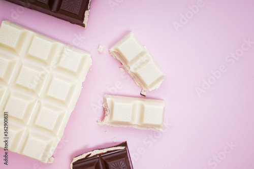 White and black chocolate bars and pieces on pink background, top view