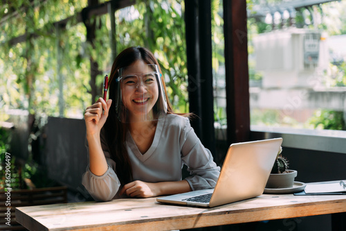 Young 20s Asian woman looking at camera while wearing a protective mask with laptop, mobile phone, notebook for working outside in casual business look. Corona Virus - Covid 19 work online concept. photo