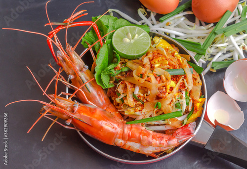Well known street food thai cuisine "Pad thai" stir fried noodles with River Prawns Serve in small red pan.