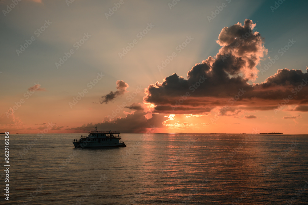 Colourful sunset in tropical islands with yacht, orange clouds and sun rays.