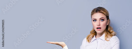 Portrait image of excited surprised blond businesswoman with opened mouth, showing something or copy space area for some imaginary, slogan or text. Success in business concept. Grey color background. photo