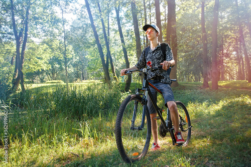 A tourist biker is sitting on a bicycle. Biker stopped in a city park against the backdrop of the setting sun and.