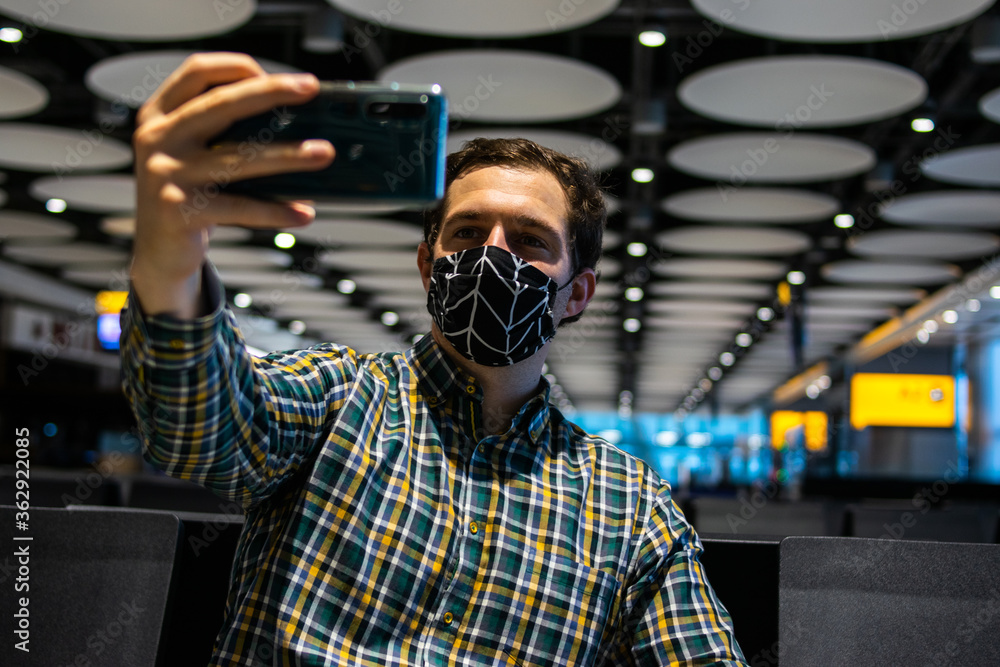 Photo of a young and attractive man taking a selfie wearing a reusable face mask while waiting to catch a flight at the airport Photo of a young and attractive man taking a selfie wearing a reusable face mask while waiting to catch a flight at the airport