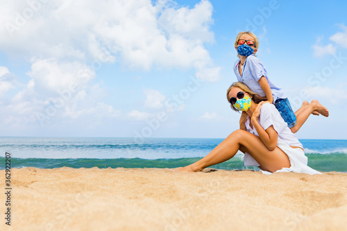 Mother, child in face masks have fun on sea beach