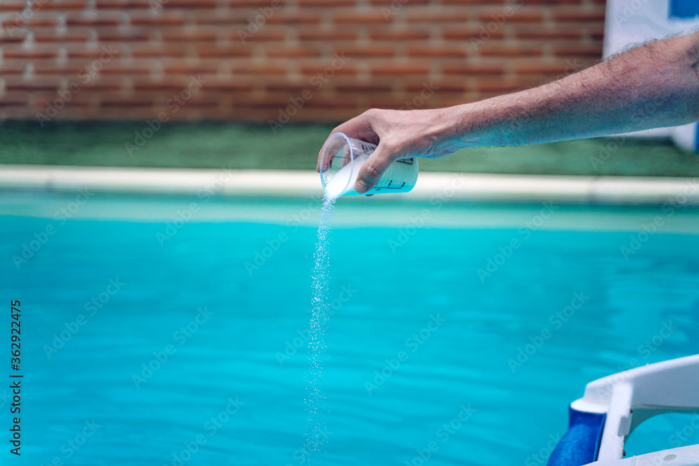 Person cleaning and chlorinating the pool on a hot summer afternoon, is