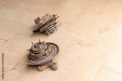 Two old, used, rusty rear hubs, on which the brake pads of the parking brake are visible, without brake disc on the beige tiled floor of the car repair shop
