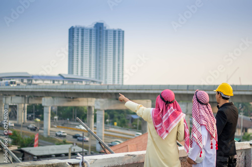 back view of arabian Investor talking with Engineer about  job progress status with blur view of main infastructure  at construction site.