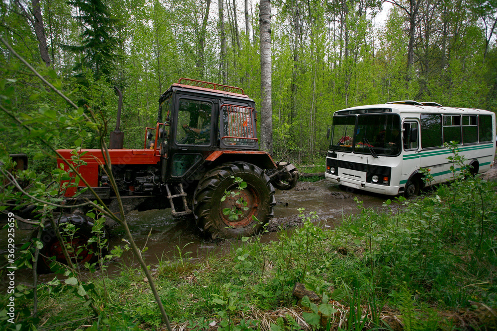 A red tractor pulls a white bus out of the mud.