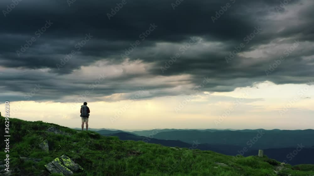 Man standing on rock with epic mountain viewpoint with a colorful sunset drone aerial landscape shot. Sun rays emerging though the dark storm clouds in the mountains Man standing on rock with epic mountain viewpoint with a colorful sunset drone aerial landscape shot. Sun rays emerging though the dark storm clouds in the mountains