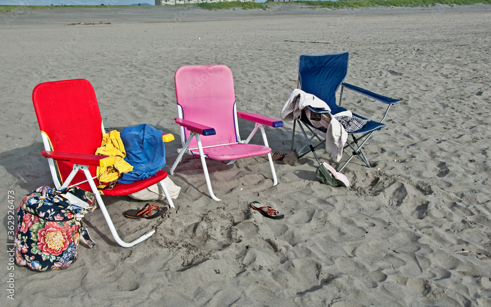 This is three colorful beach chairs, with various beach items left behind, clothing, sandals, bags, phones on a sandy beach. Great vacation image. This is three colorful beach chairs, with various beach items left behind, clothing, sandals, bags, phones on a sandy beach. Great vacation image.