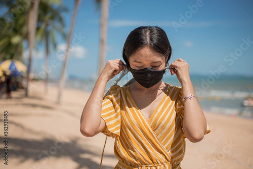 Asian woman wearing protective face mask on the beach,  newnormal lifestyle after Coronavirus pandemic. photo