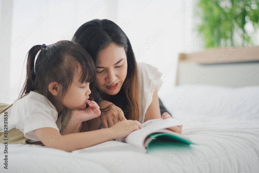 Love of young Asian mother and daughter. Teaching reading a homework or book on the white bed at home. daughter look the book and learning study at home felling be serious. Asian love family concept. Love of young Asian mother and daughter. Teaching reading a homework or book on the white bed at home. daughter look the book and learning study at home felling be serious. Asian love family concept.